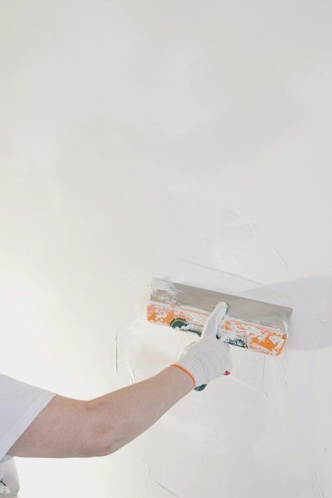 Close-up of a gloved hand plastering a wall with a spatula in a home renovation setting.